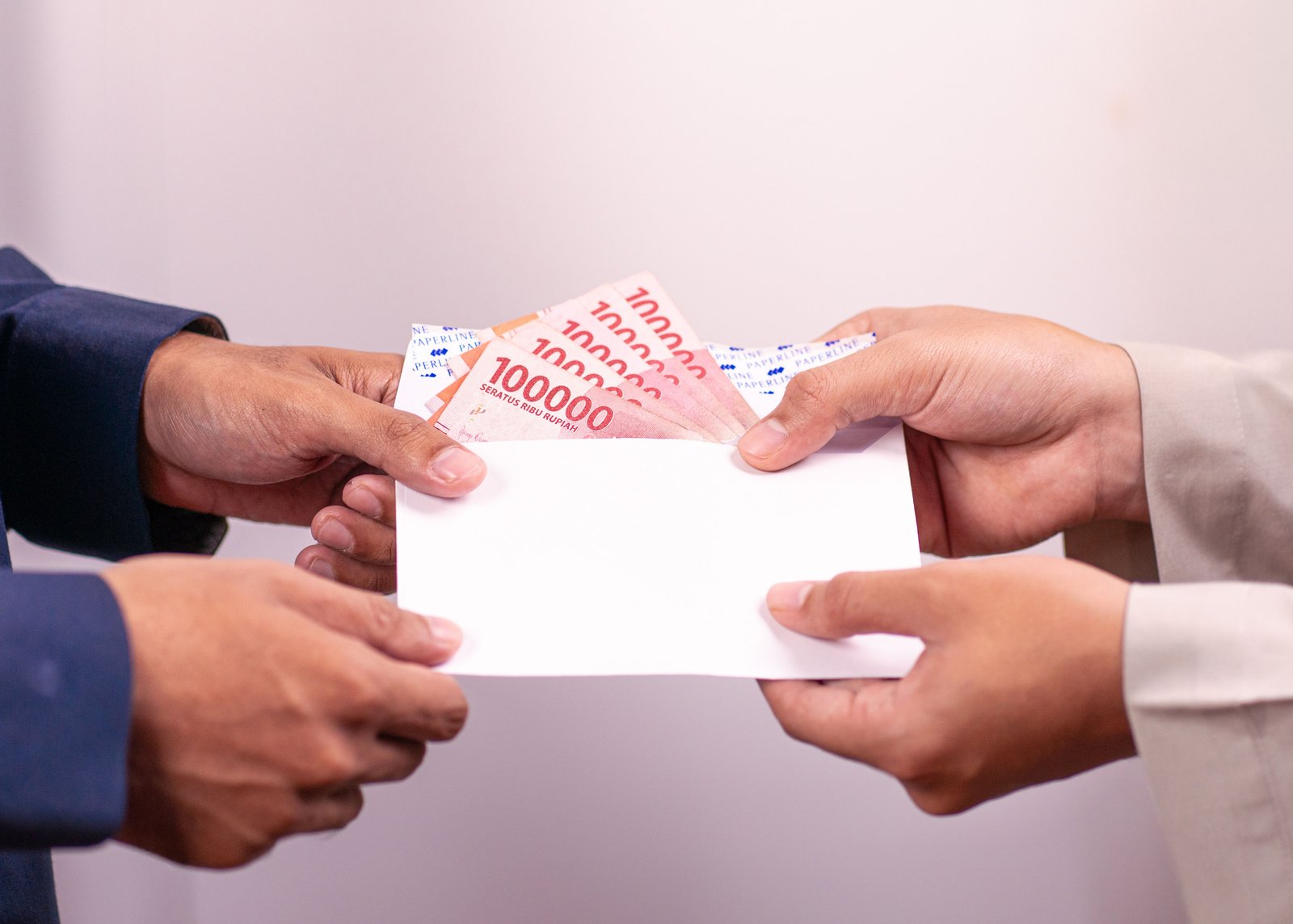 Hands exchanging an envelope with Indonesian Rupiah, highlighting financial transactions.