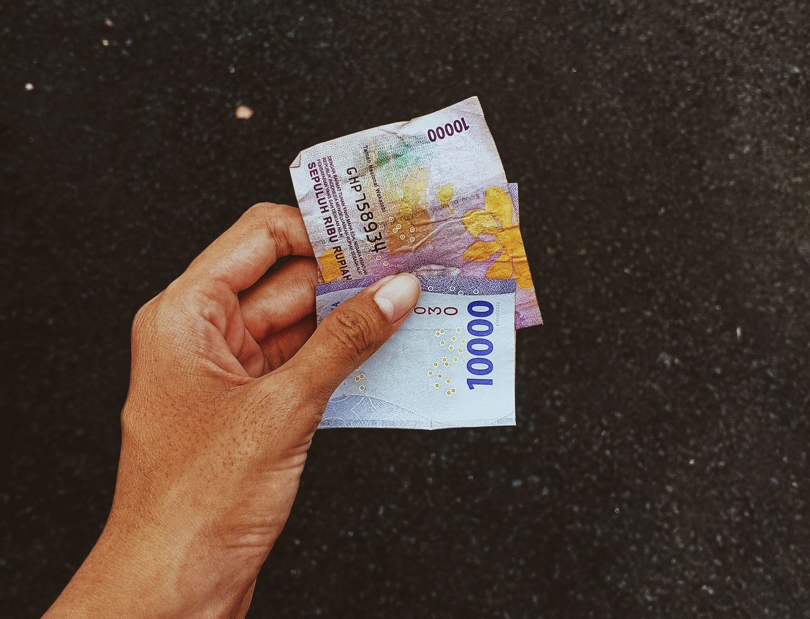 A close-up of a hand holding currency notes against a dark surface, emphasizing finance and economy.